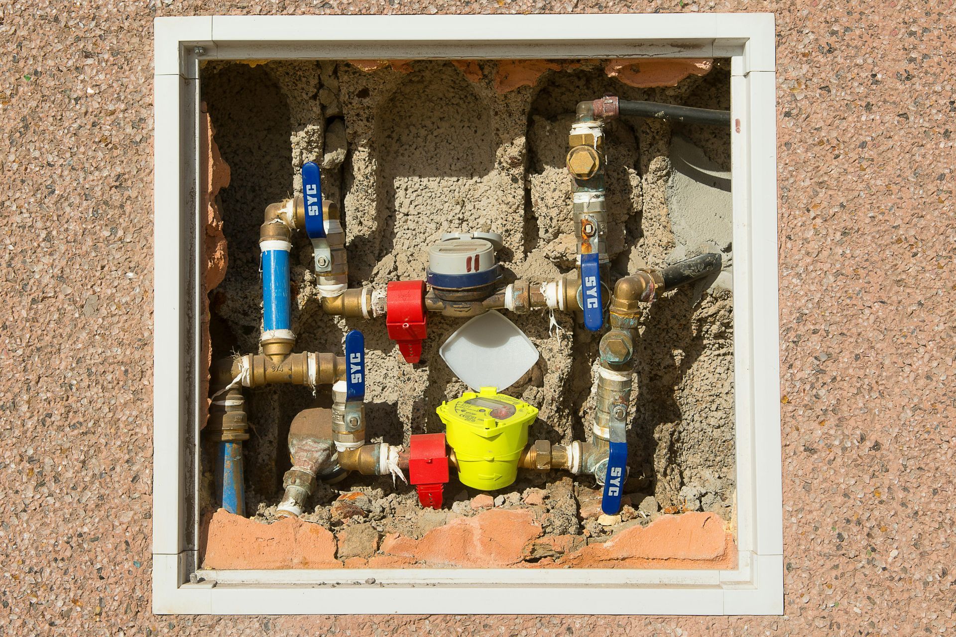 Water meter and pipes within a recessed outdoor wall, blue and red valves.