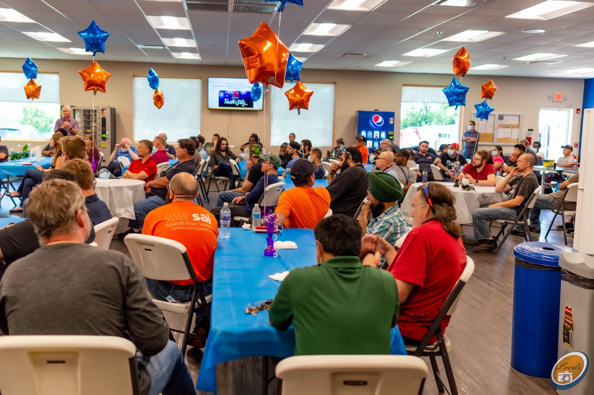 People seated around tables in a decorated community room for a gathering or meeting