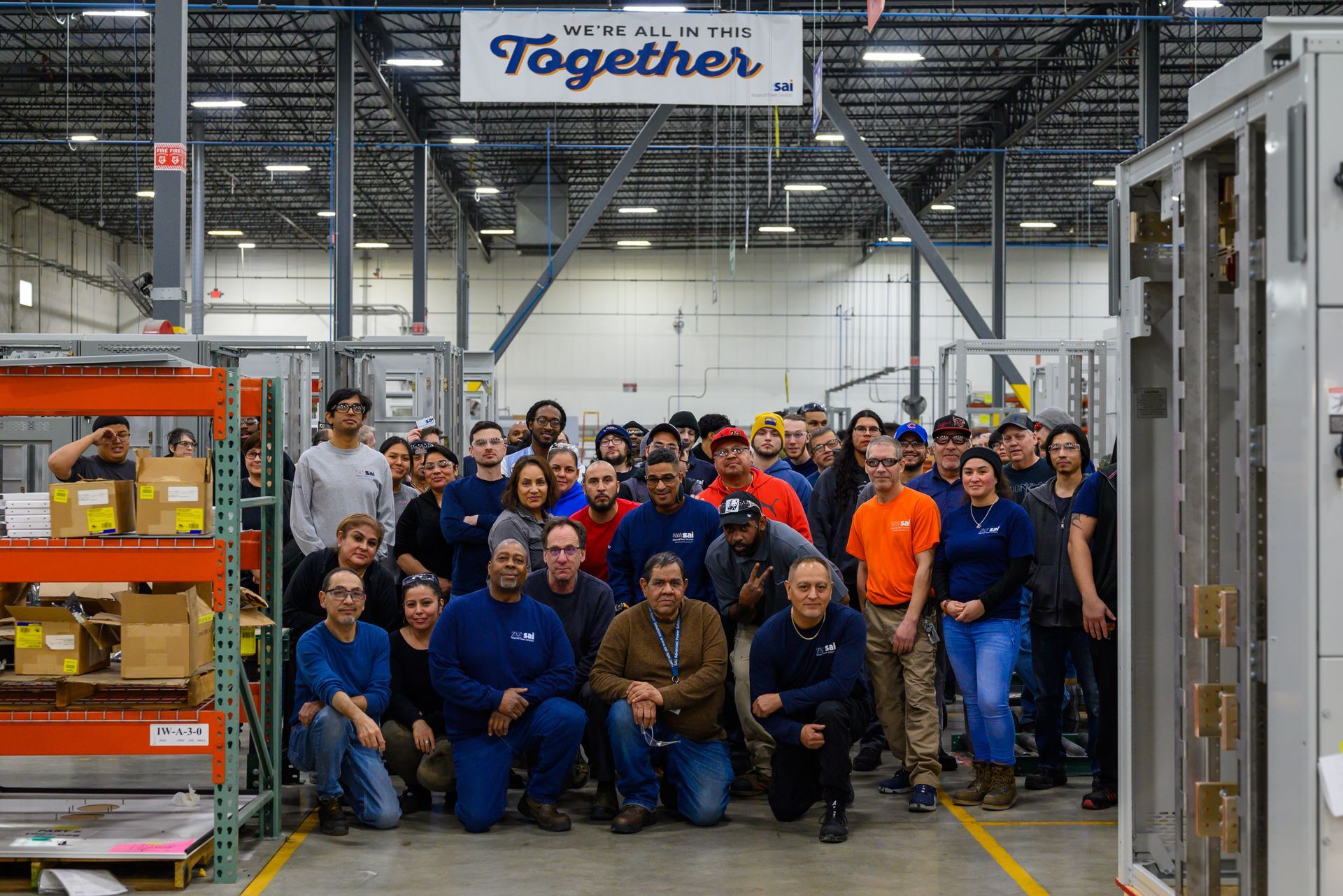Factory team posing together in an industrial warehouse, with a “Together” banner overhead.