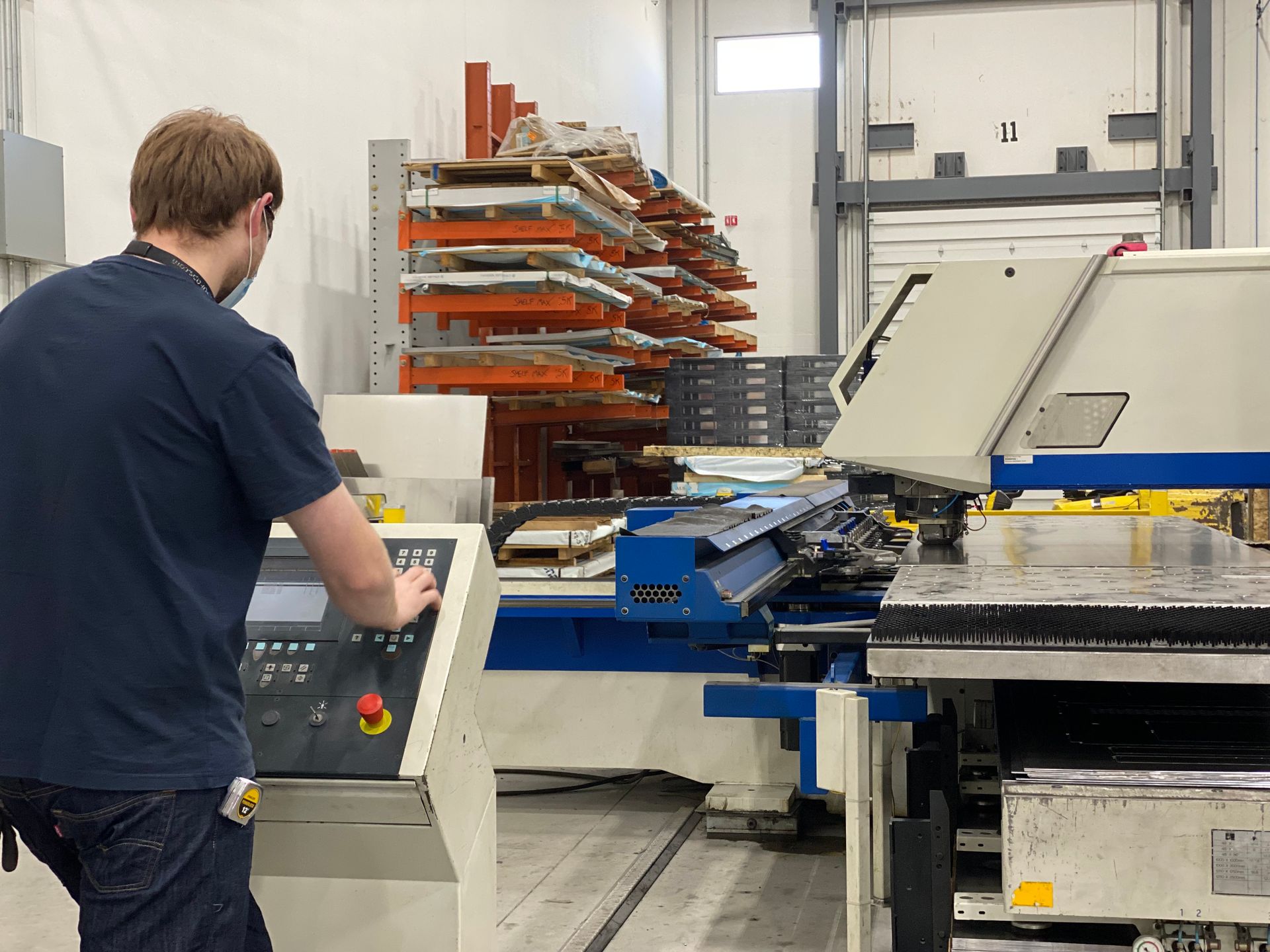 Worker operating a control panel beside a large industrial printing press in a workshop