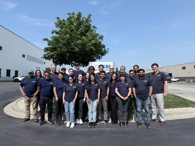 Group of people in navy shirts posing outdoors in front of a building and tree