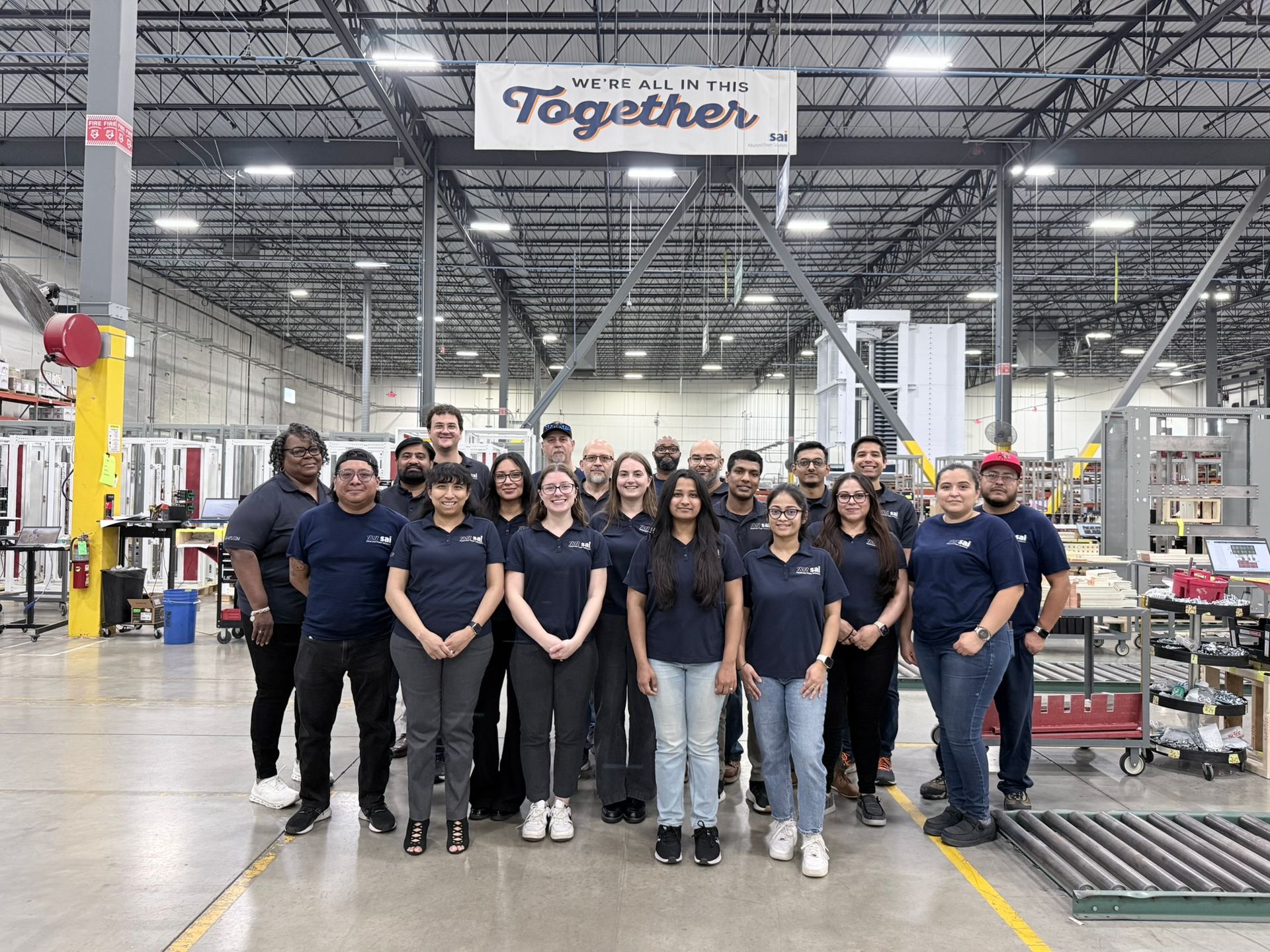 Group of employees standing together in a warehouse aisle under a “Together” banner