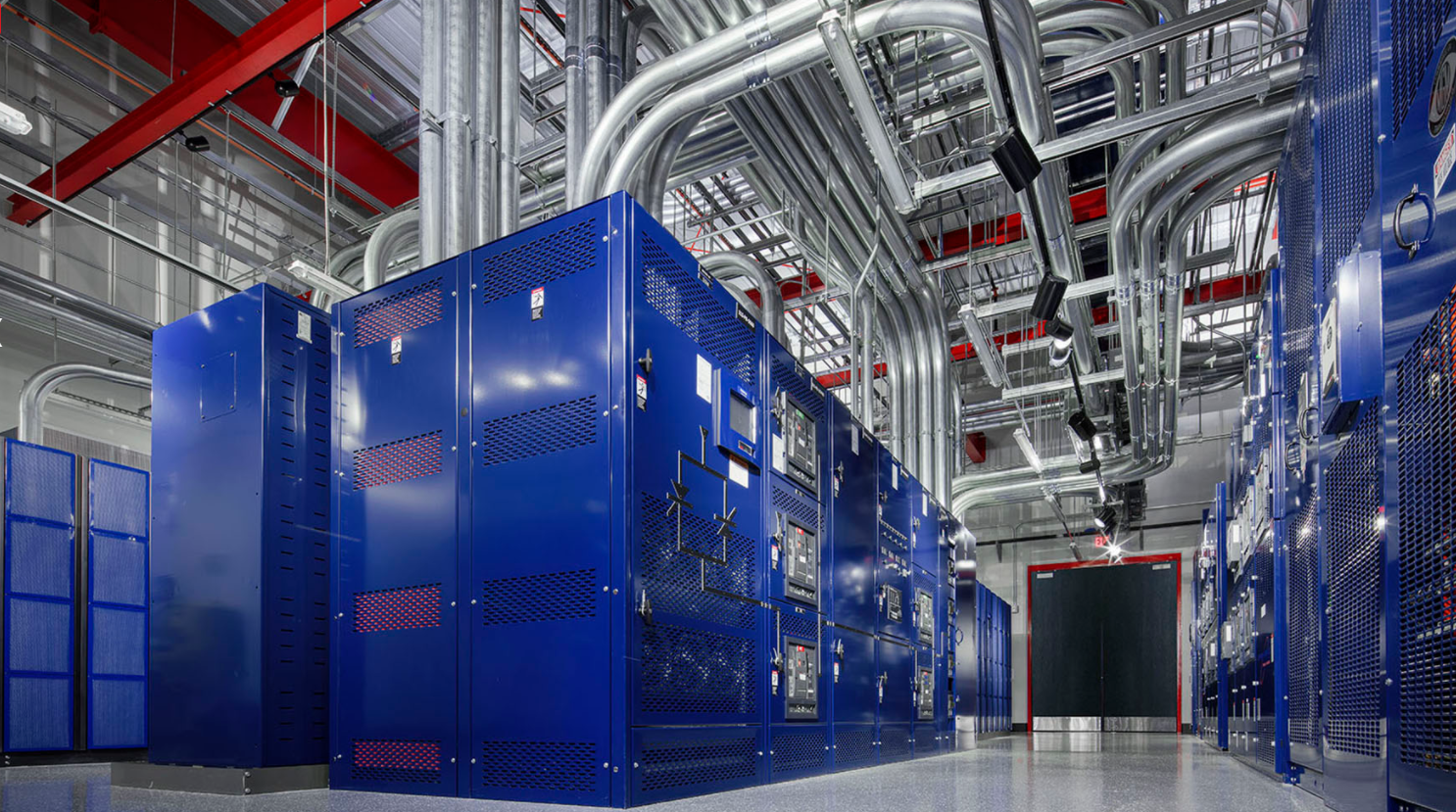 Blue server racks in a modern data center with bright overhead piping and industrial lighting