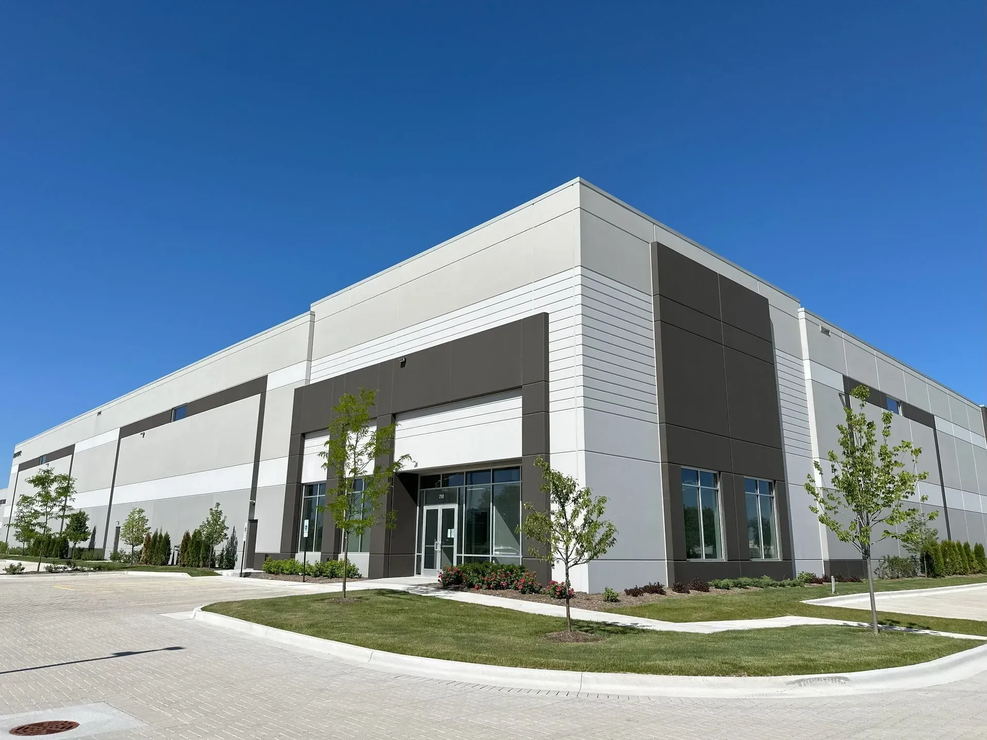 Modern gray commercial building with glass entrance and parking lot under a blue sky