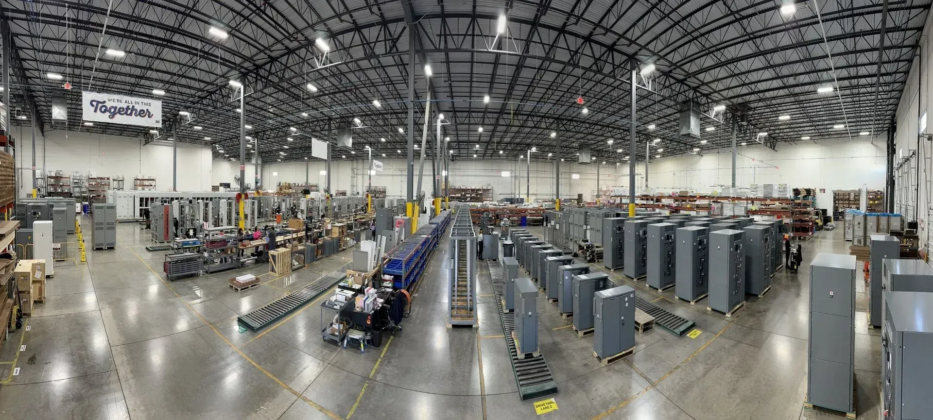 Wide indoor warehouse or convention hall with rows of equipment and people working under a high arched ceiling