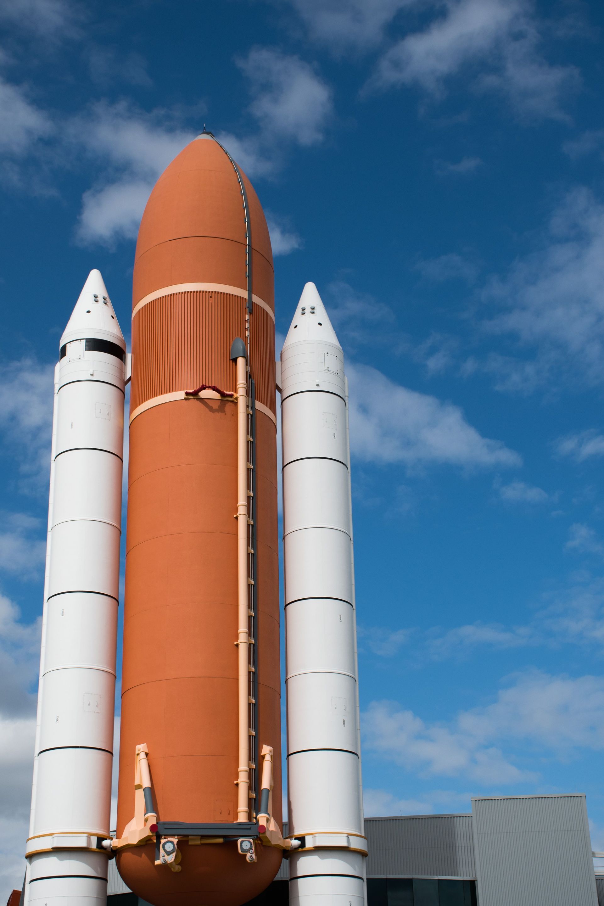 Space shuttle on launch pad against blue sky, with orange orbiter and white boosters.