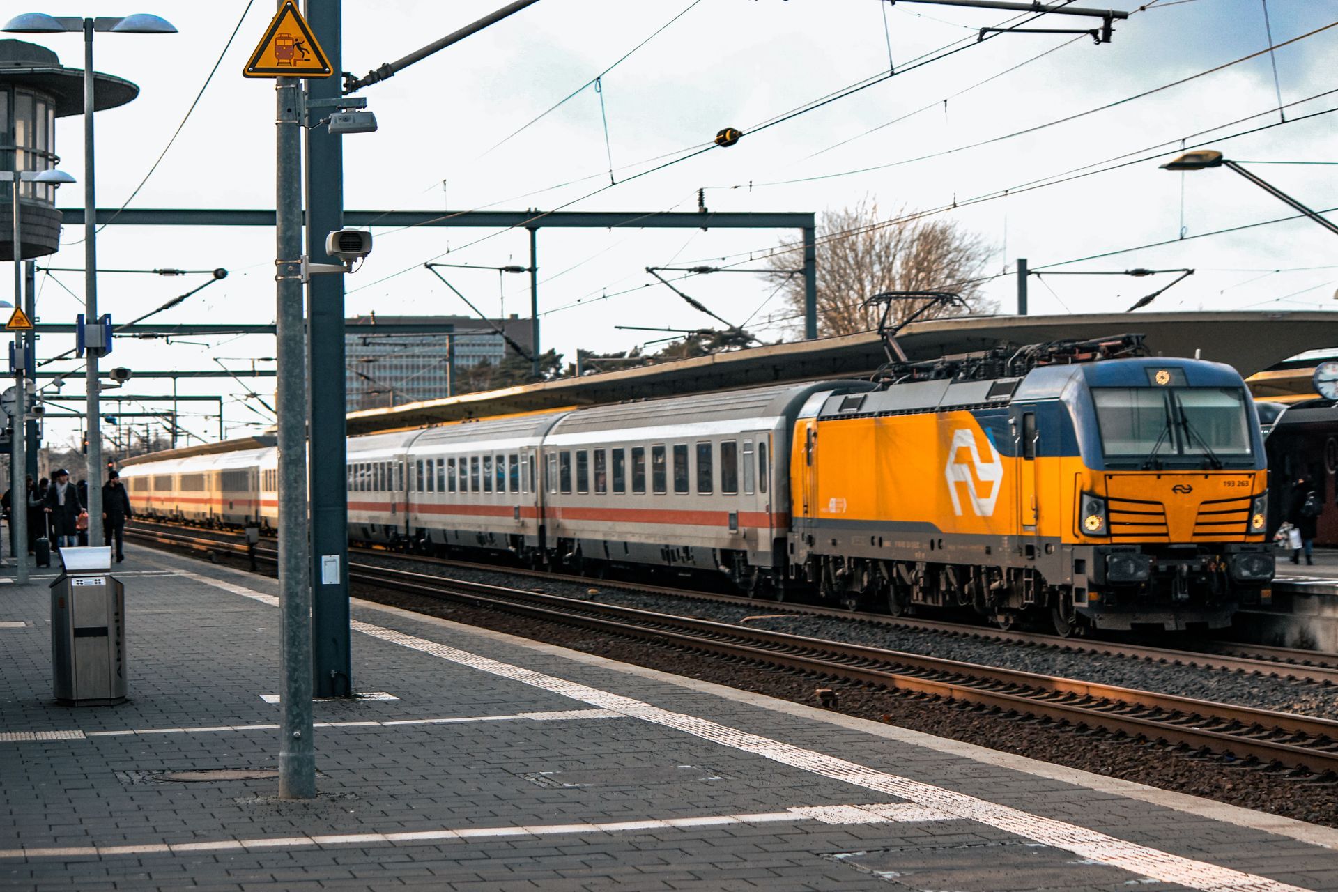 Orange and white passenger train at a station platform under overhead wires