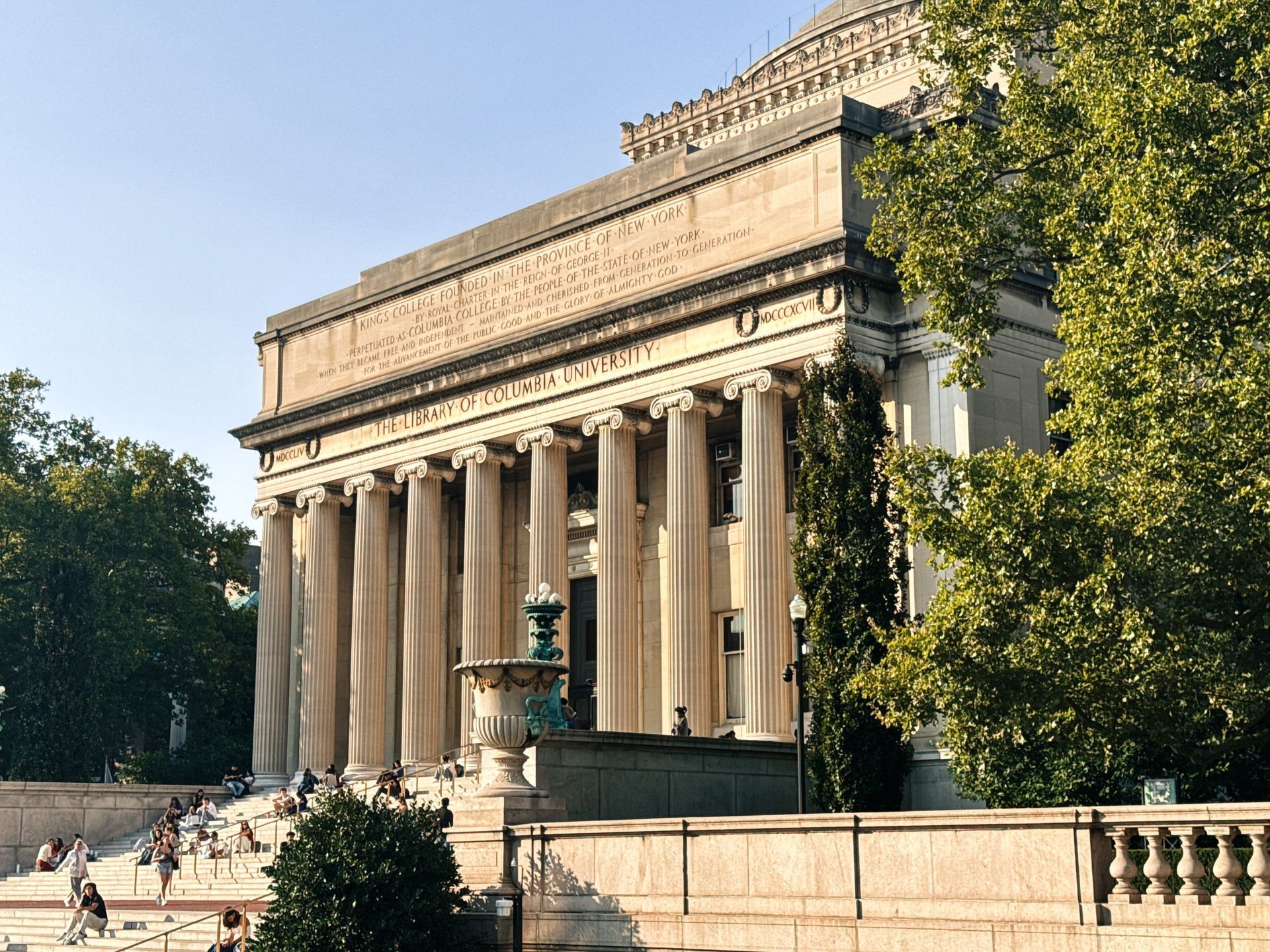 Grand stone museum with tall columns and a fountain in front, surrounded by trees on a sunny day