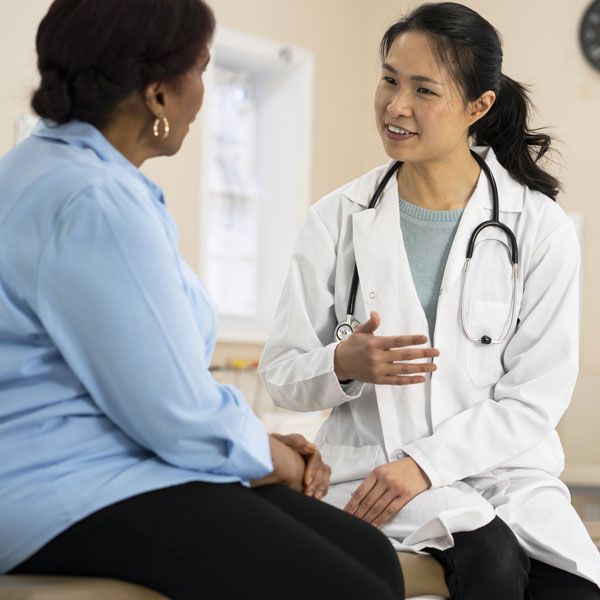 Doctor in white coat talking with seated patient in a clinic office