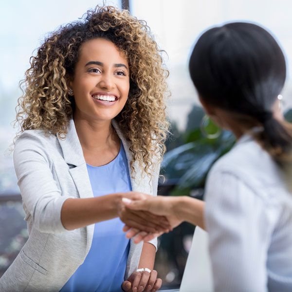 Two people shaking hands in a bright office, one smiling at a desk