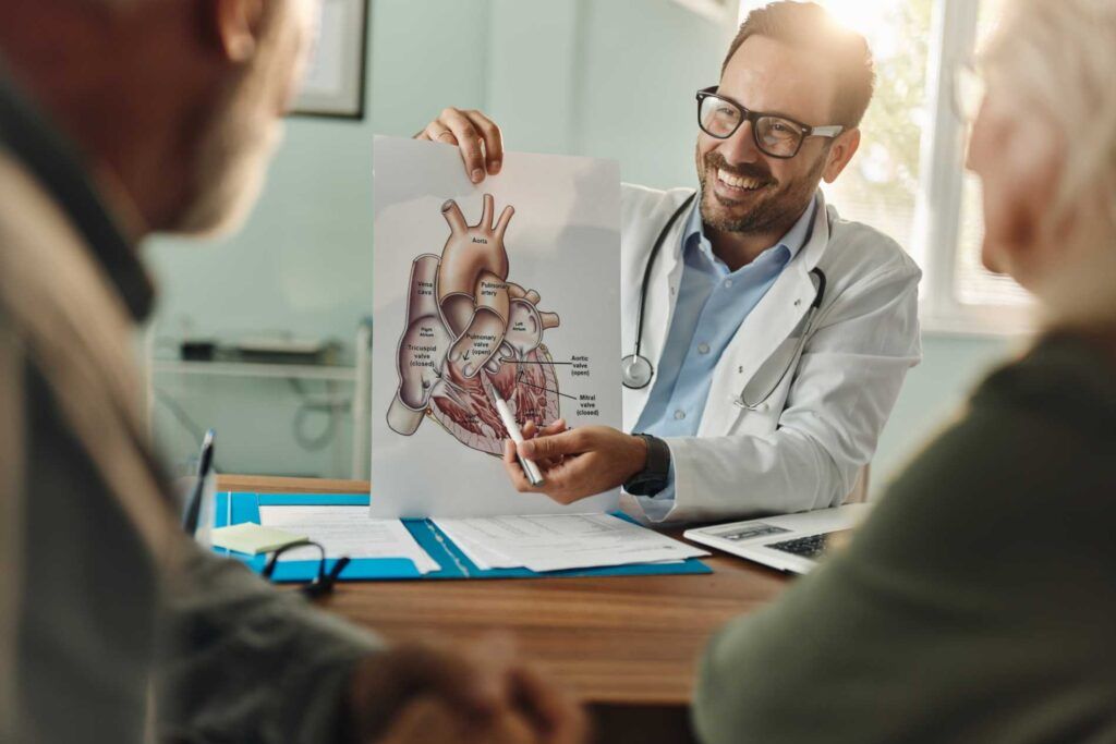 Doctor showing a heart diagram to two seated people in a clinic meeting