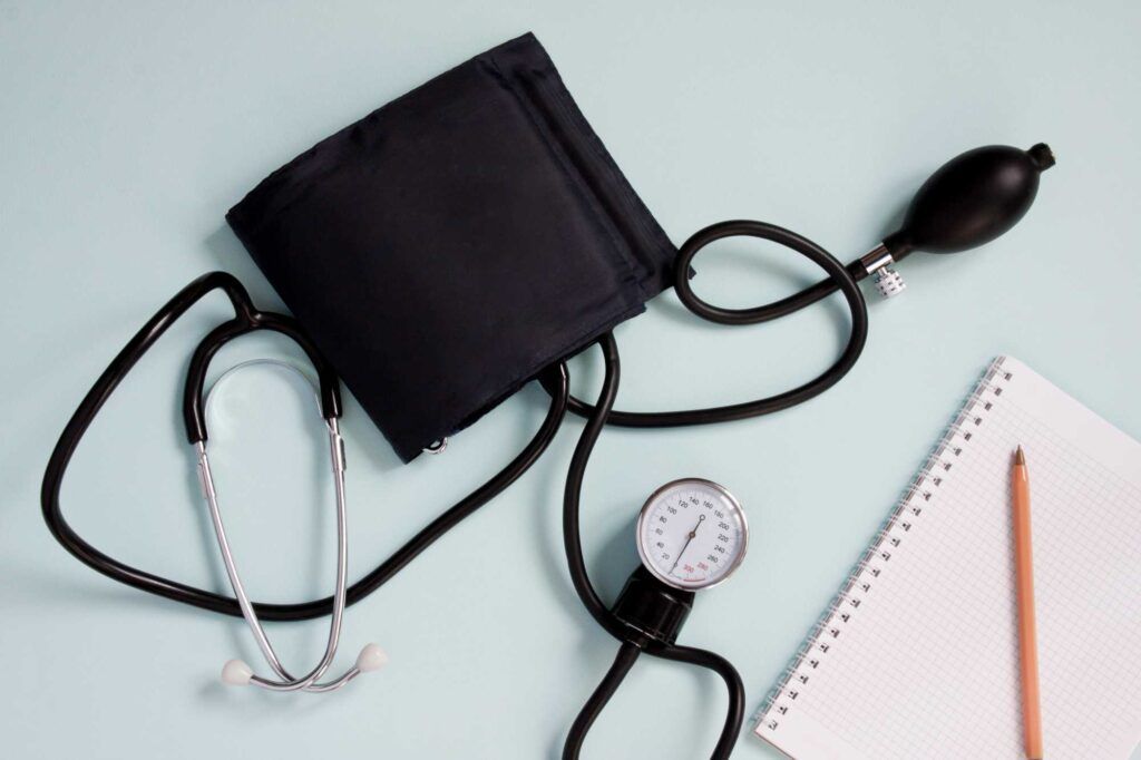 Blood pressure cuff and stethoscope on a light desk beside a notebook and pencil