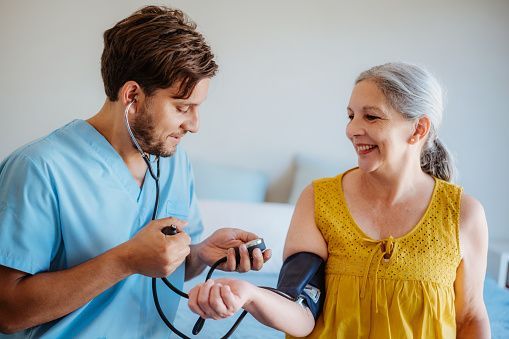 Nurse taking a woman’s blood pressure while smiling in a bright clinic room
