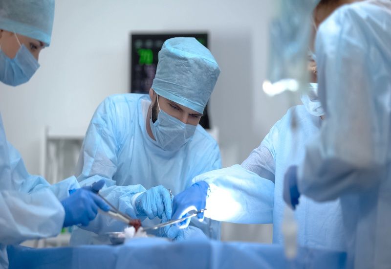 Surgeons in blue protective gear performing an operation under bright operating room lights