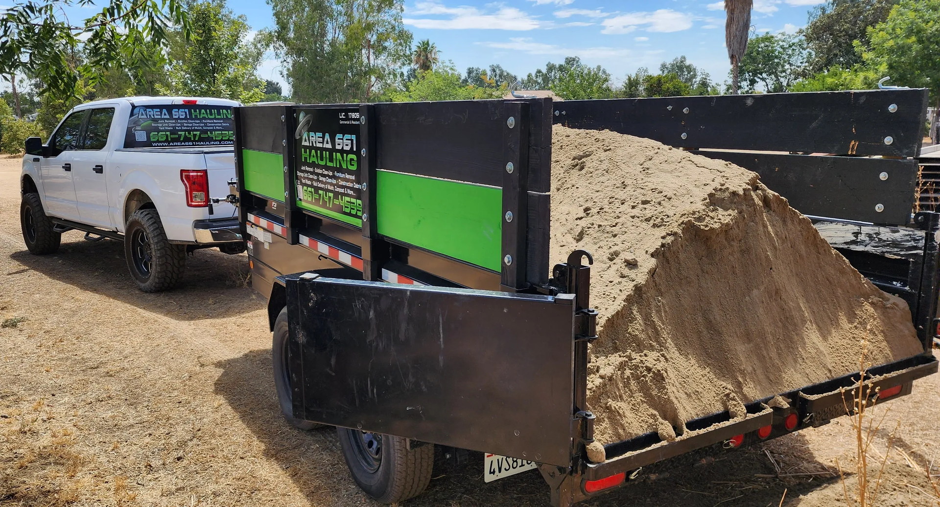 A white truck is towing a trailer filled with sand.