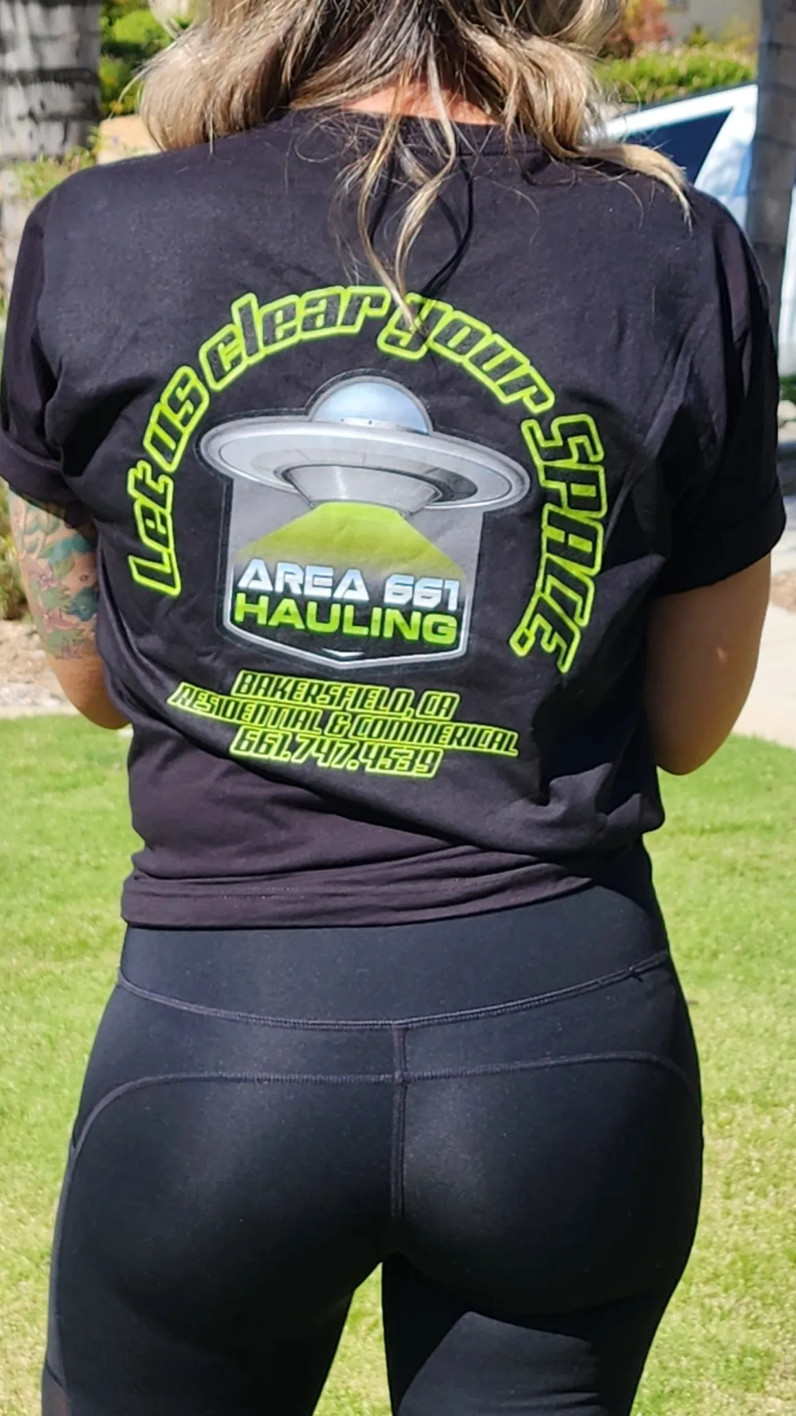The back of a woman wearing a black t-shirt with Area 661 Hauling logo on it.