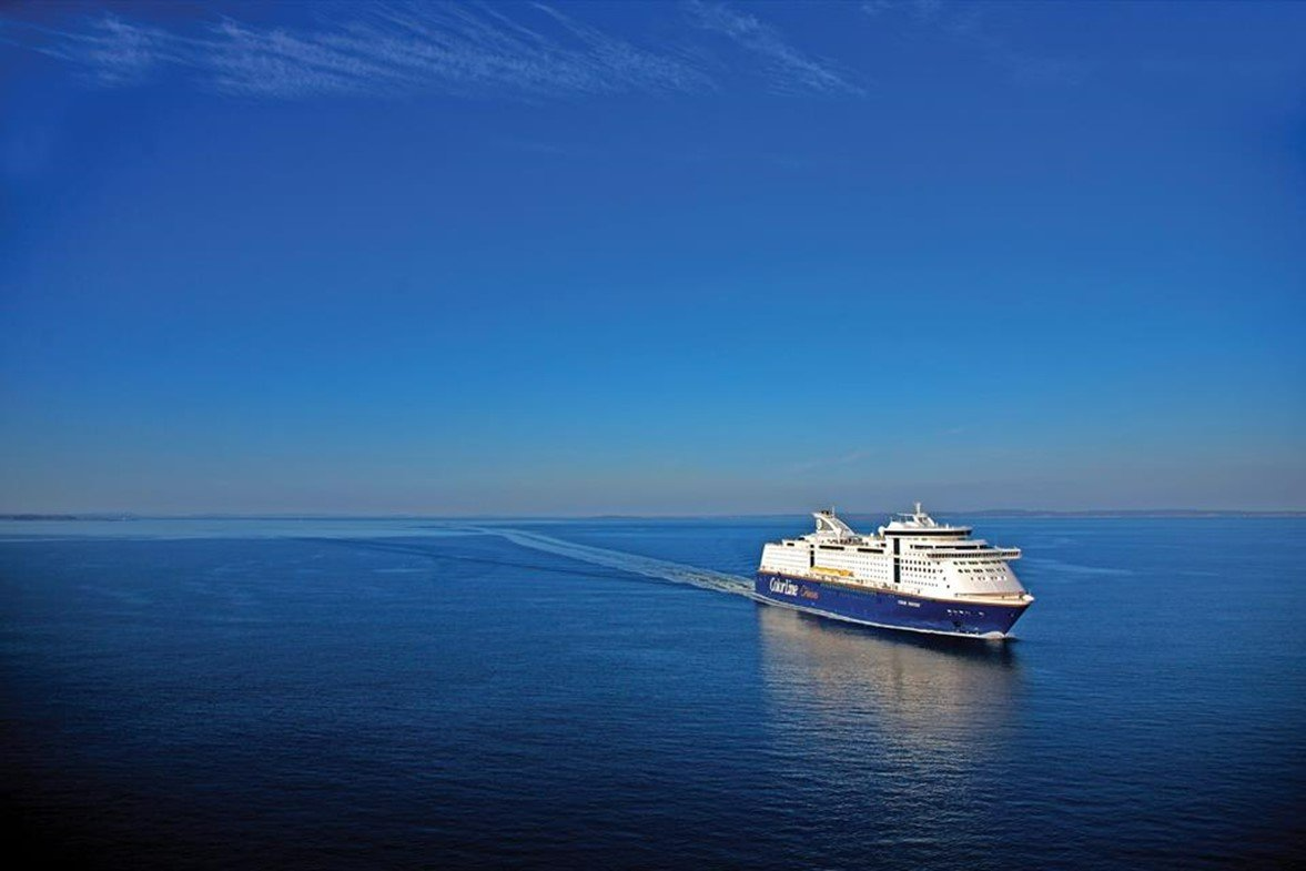 Cruiseskip på blått vann under klar himmel, etterlater et hvitt kjølvann.