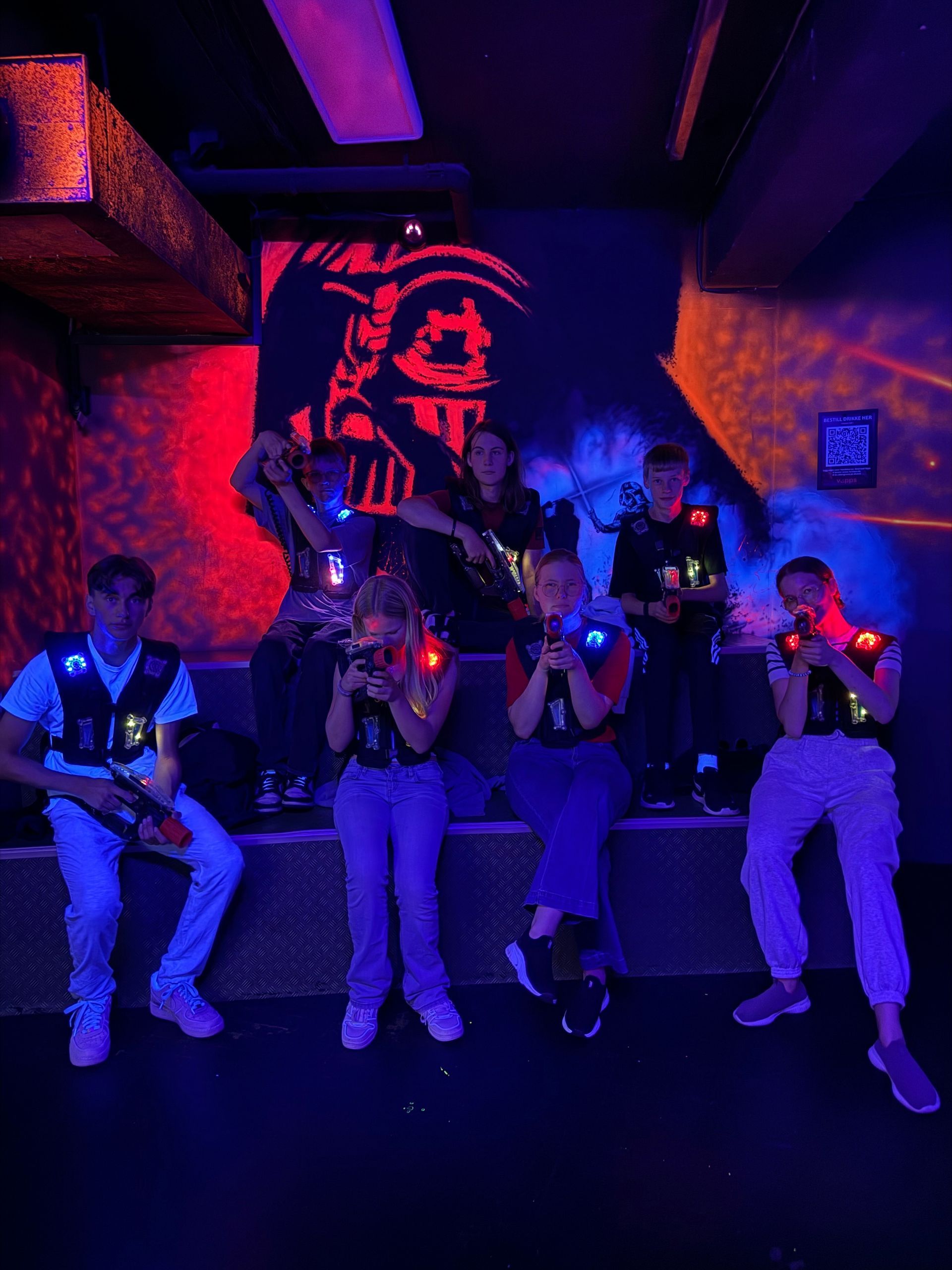 Folk spiller laser tag i et svakt opplyst rom med røde og blå lys.