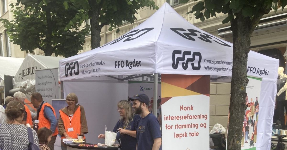Folk ved et hvitt telt med skiltingen «FFO Agder». En kvinne og en mann står ved et bord og deler ut informasjon.
