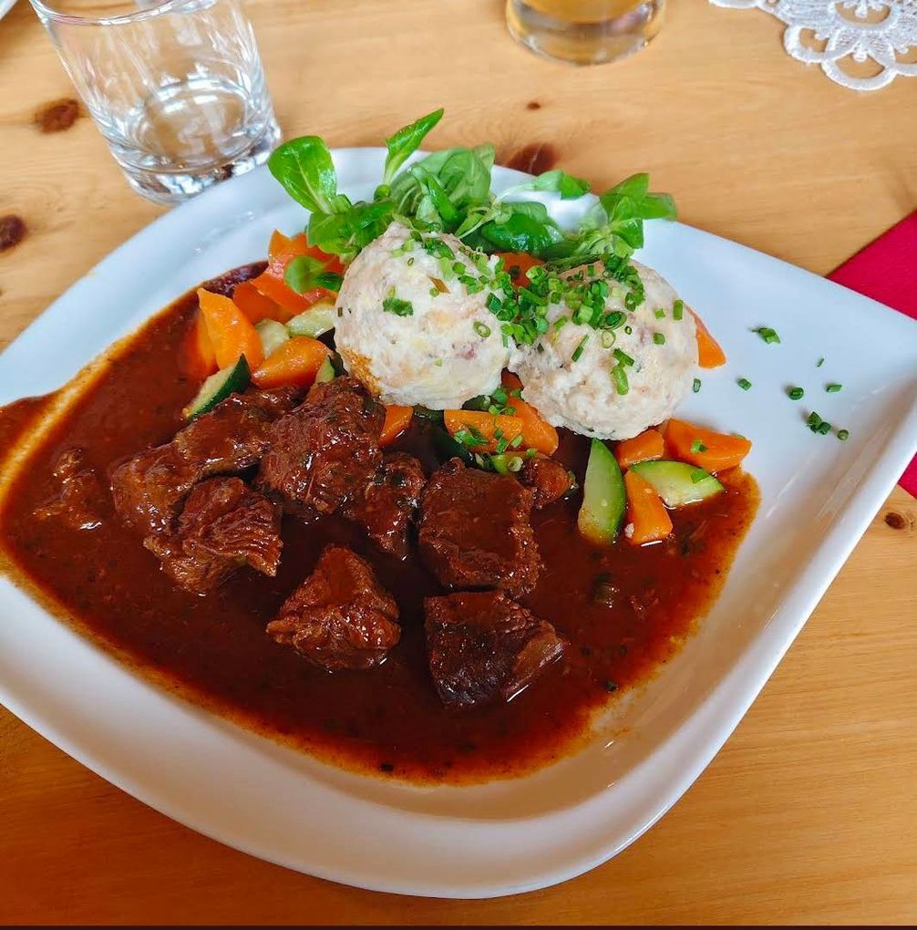 Bistecca grigliata e tagliata a fette con interno rosa, patate, spicchio di limone e rucola su un piatto bianco.