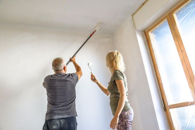 A man and a woman are painting the ceiling of a room.