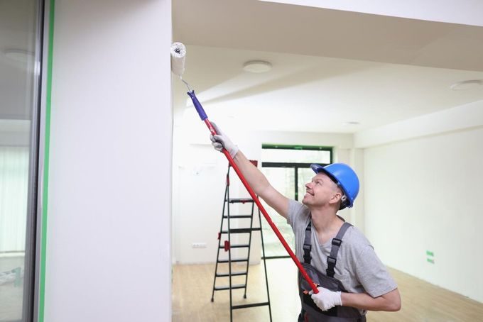 A man is painting a wall with a paint roller.