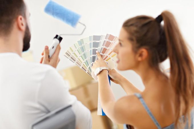A man and a woman are looking at paint samples while painting a wall.
