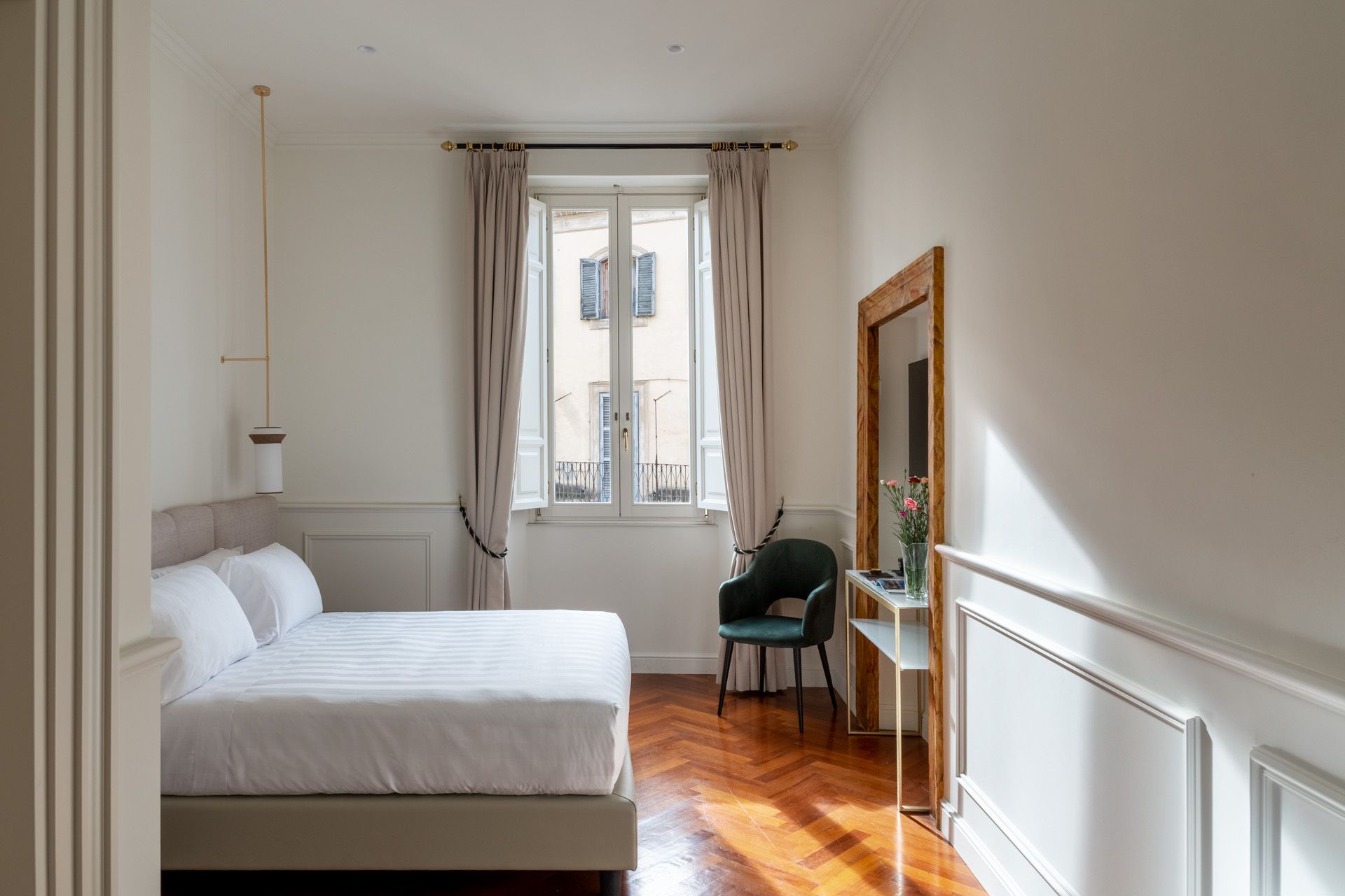 Bedroom with a bed, large mirror, and a window. Sunlight streams across the wooden floor.