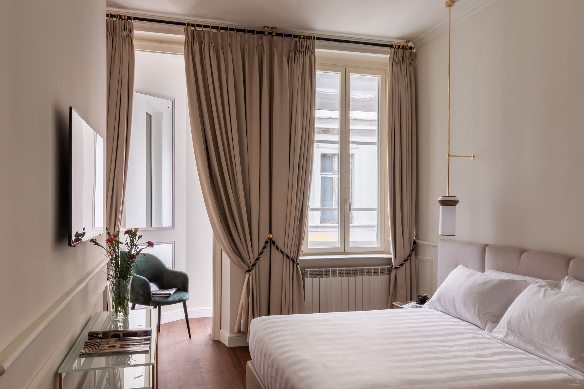 Bedroom with bed, drapes, window, chair, TV, and decorative vase. Neutral colors, modern design.