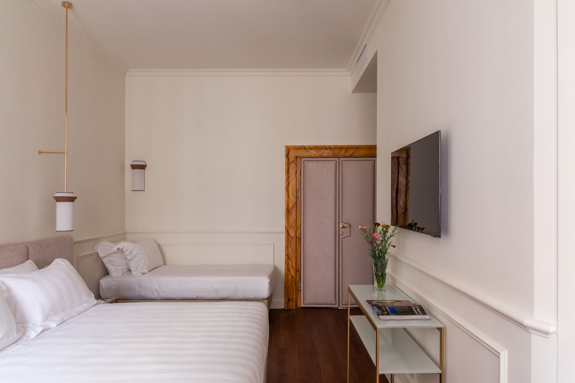 Bedroom with white walls, a bed, a pull-out couch, a TV, and a door with wooden trim.