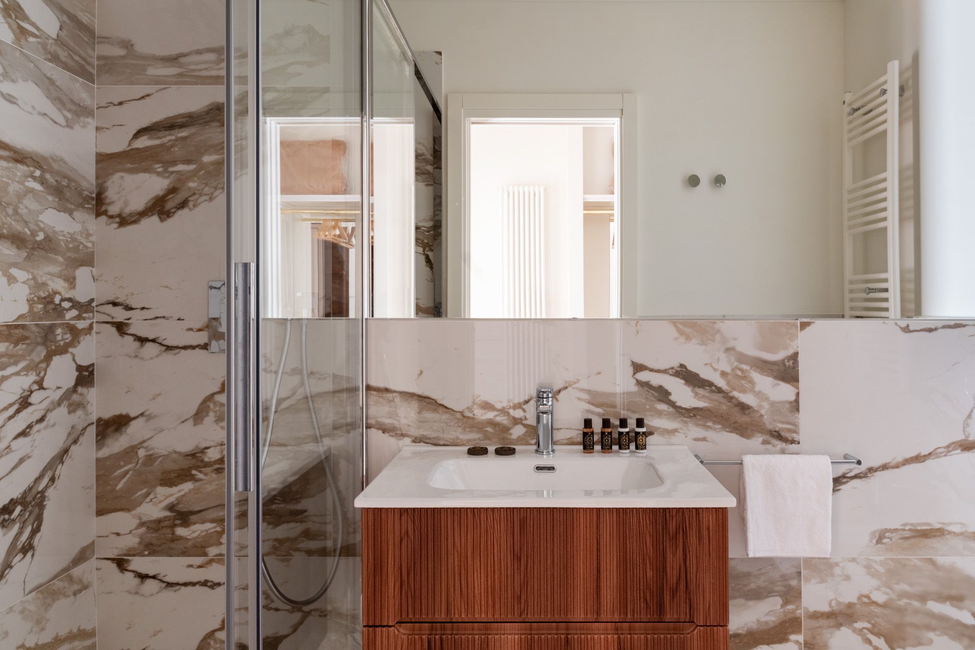Bathroom with marble walls and wooden vanity. Shower stall on the left. Towel hangs on the right.