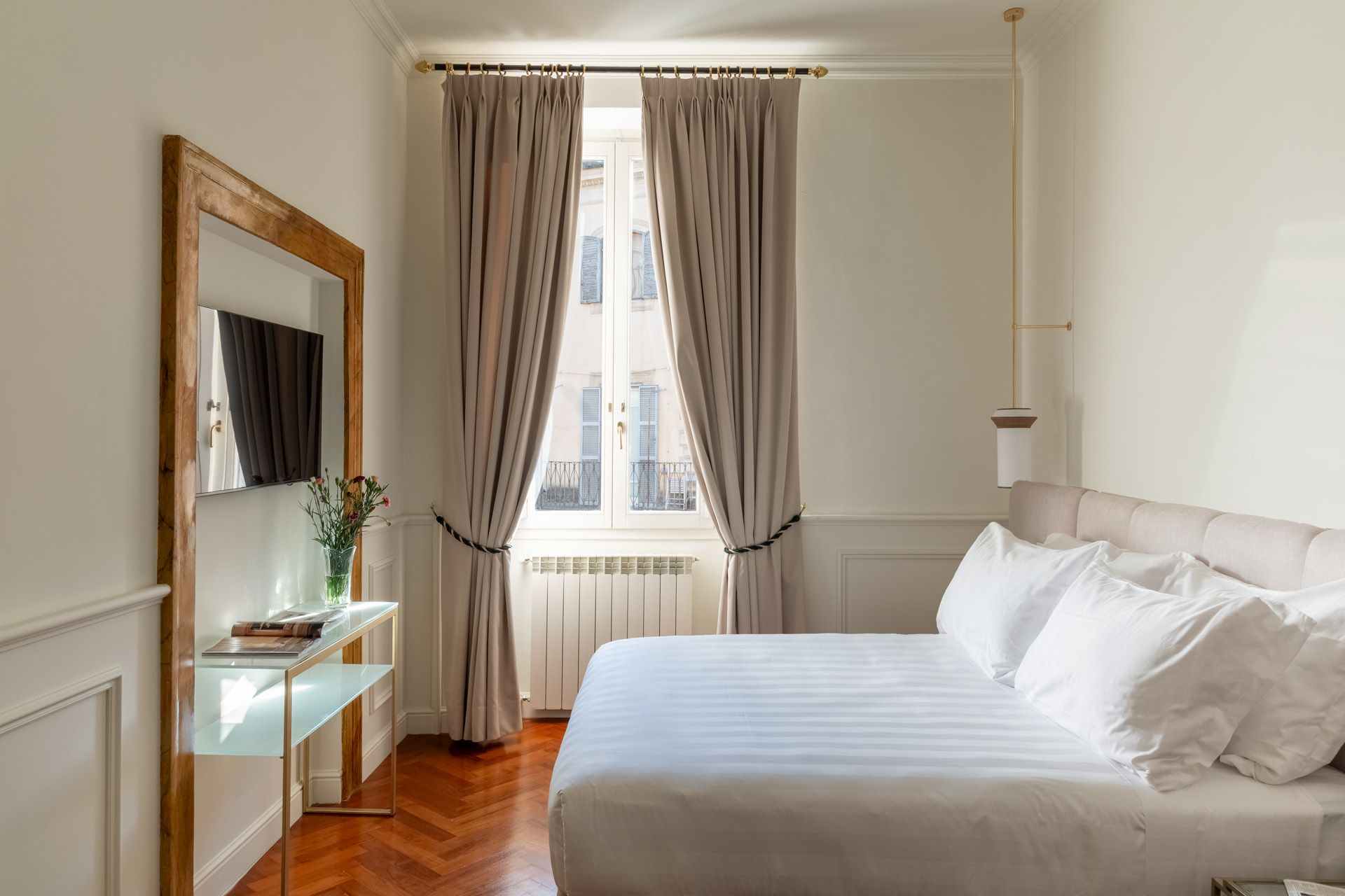 Bedroom with a bed, window with curtains, a mirror, and a small table.