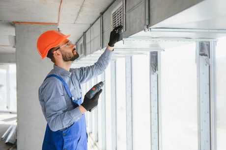 Construction worker in orange hard hat inspecting ceiling fixtures in a bright unfinished room