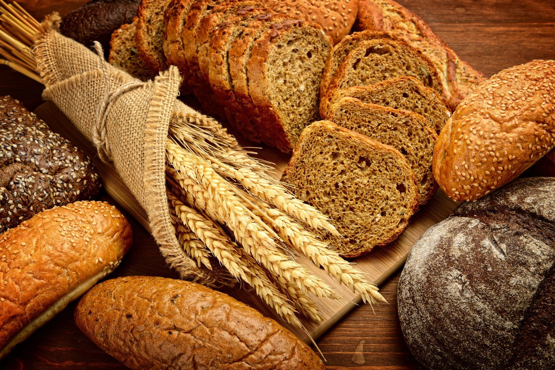 Pane rustico assortito e spighe di grano su un tavolo di legno, in calde tonalità dorate