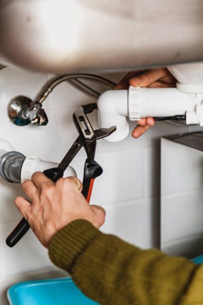 Close-up of plumber’s hands as they fix a PVC pipe with a wrench, inside a kitchen.
