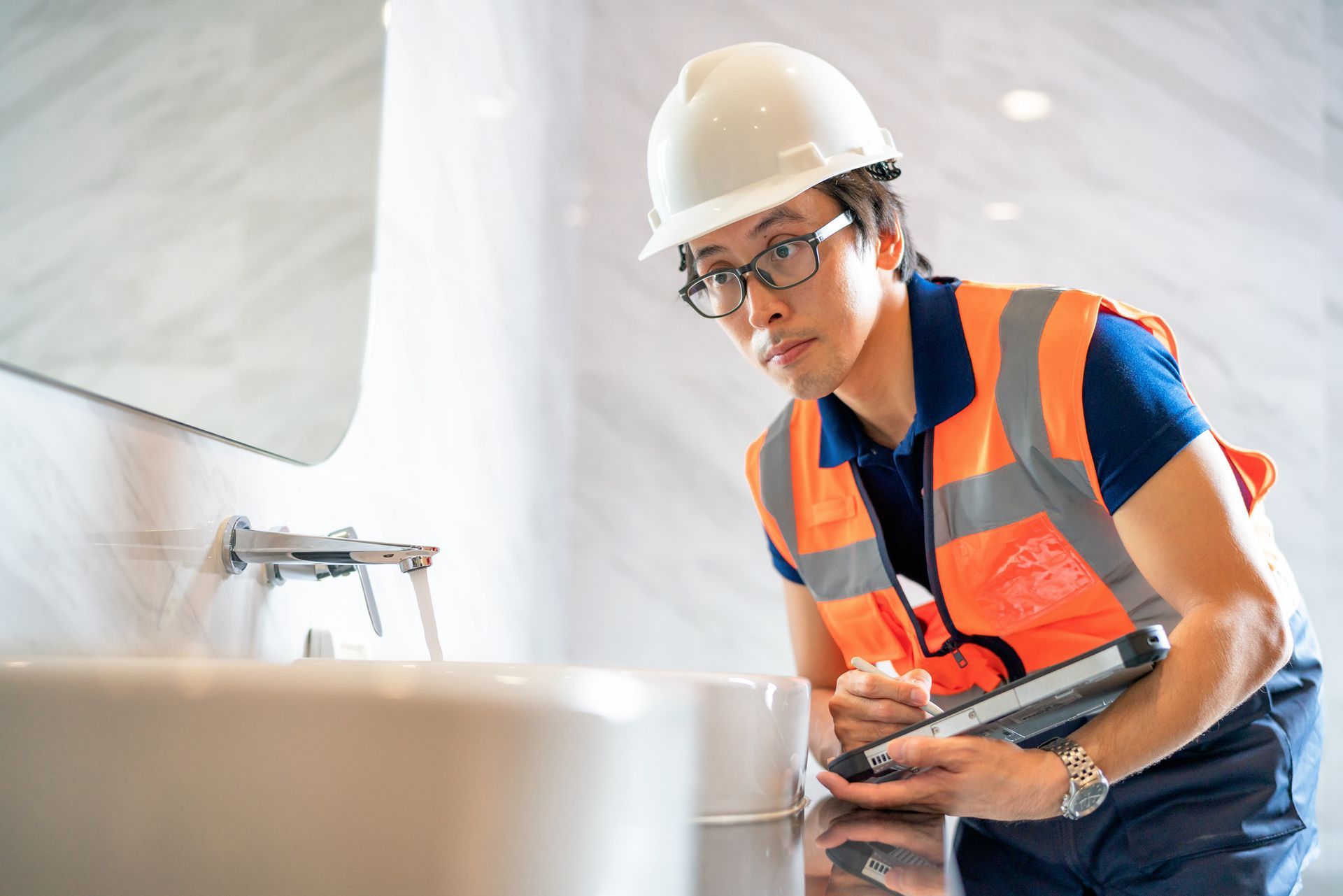 Construction worker in safety gear inspecting a bathroom sink. Construction worker in safety gear inspecting a bathroom sink.
