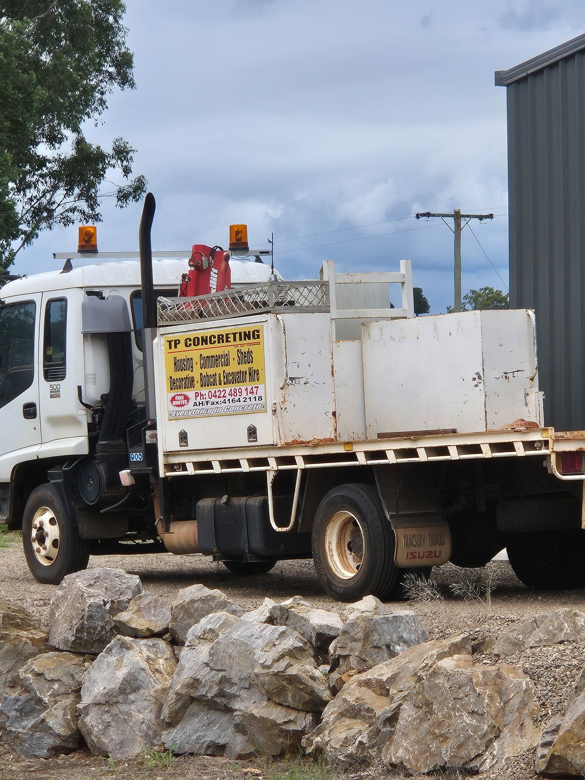 White Utility Truck Parked on Rocks Beside a Metal Building — TP Concreting In Warilla, NSW
