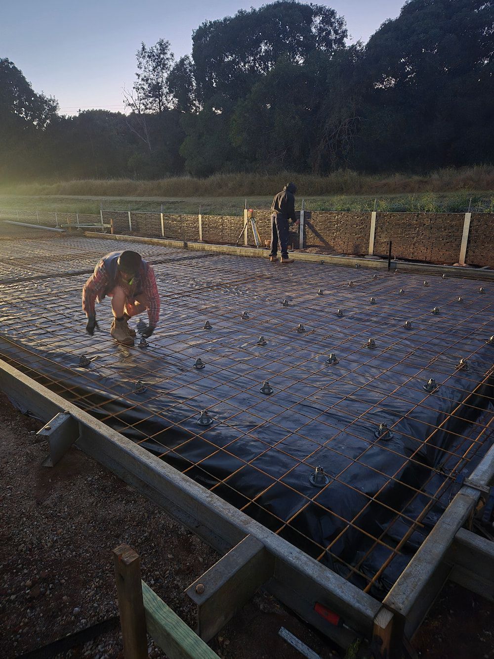 Workers Tying Rebar Over a Concrete Foundation Slab at Dusk — TP Concreting In Albion Park, NSW