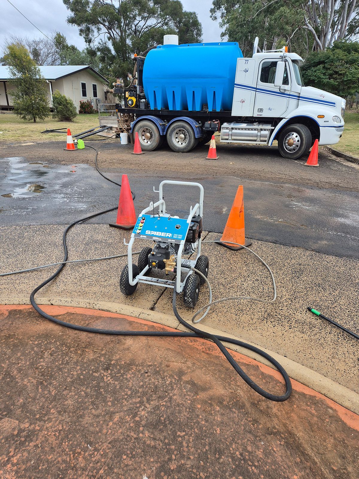 Blue Utility Truck and Pressure Washer Setup on a Wet Street With Traffic Cones and Hoses — TP Concreting In Warilla, NSW