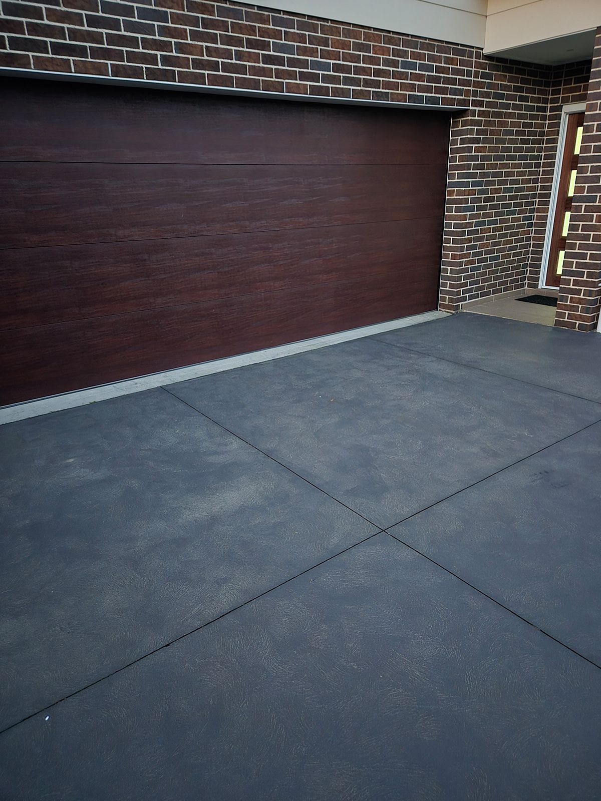 Brick House Garage With a Closed Maroon Door and a Dark Concrete Driveway — TP Concreting In Warilla, NSW