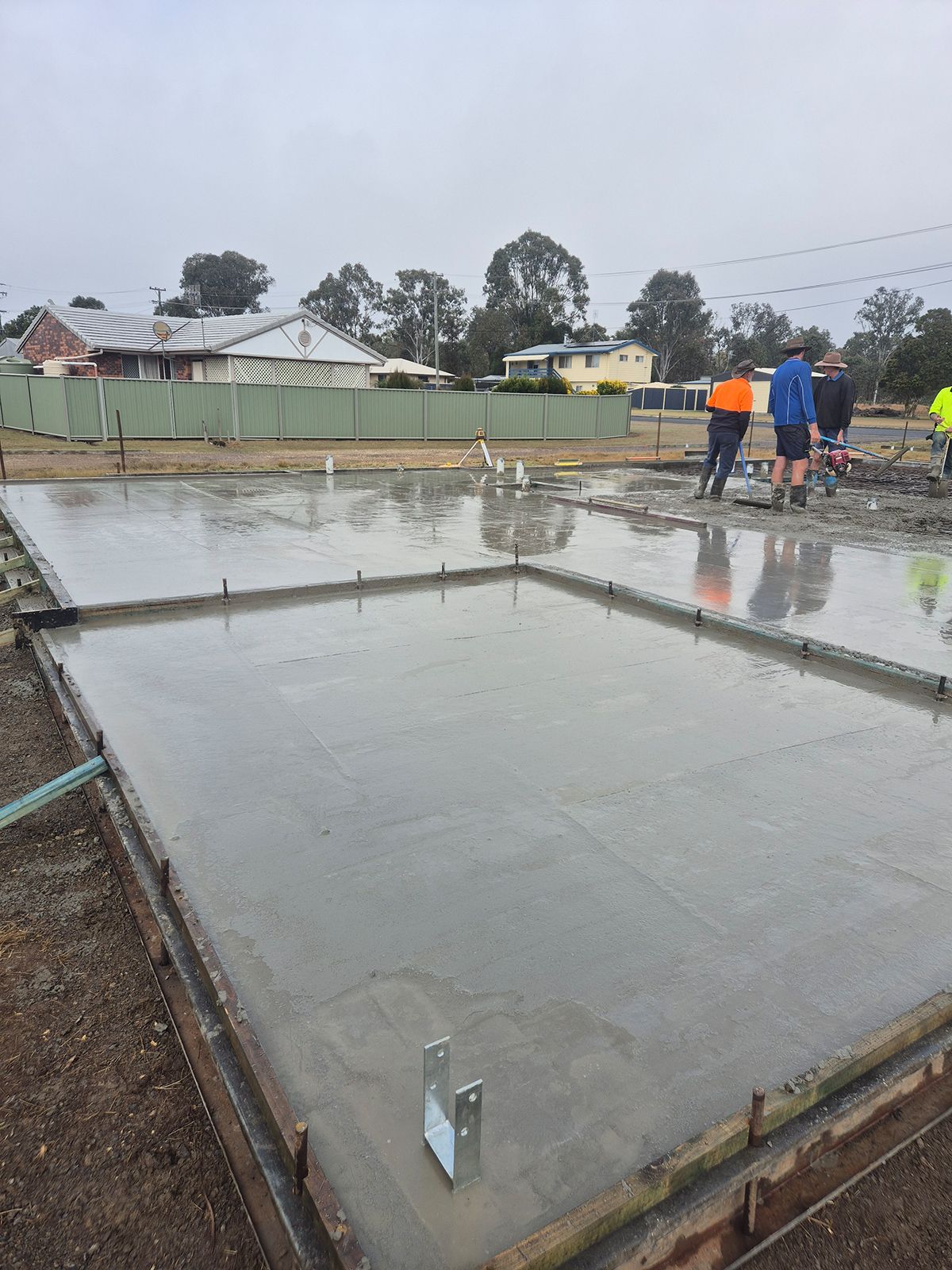 Workers Smoothing Wet Concrete on a Large Foundation Slab at a Rainy Construction Site — TP Concreting In Warilla, NSW