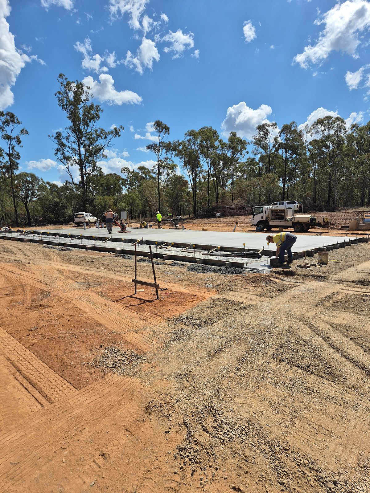 Construction Workers Pouring a Concrete Slab at a Wooded Building Site Under a Blue Sky — TP Concreting In Warilla, NSW