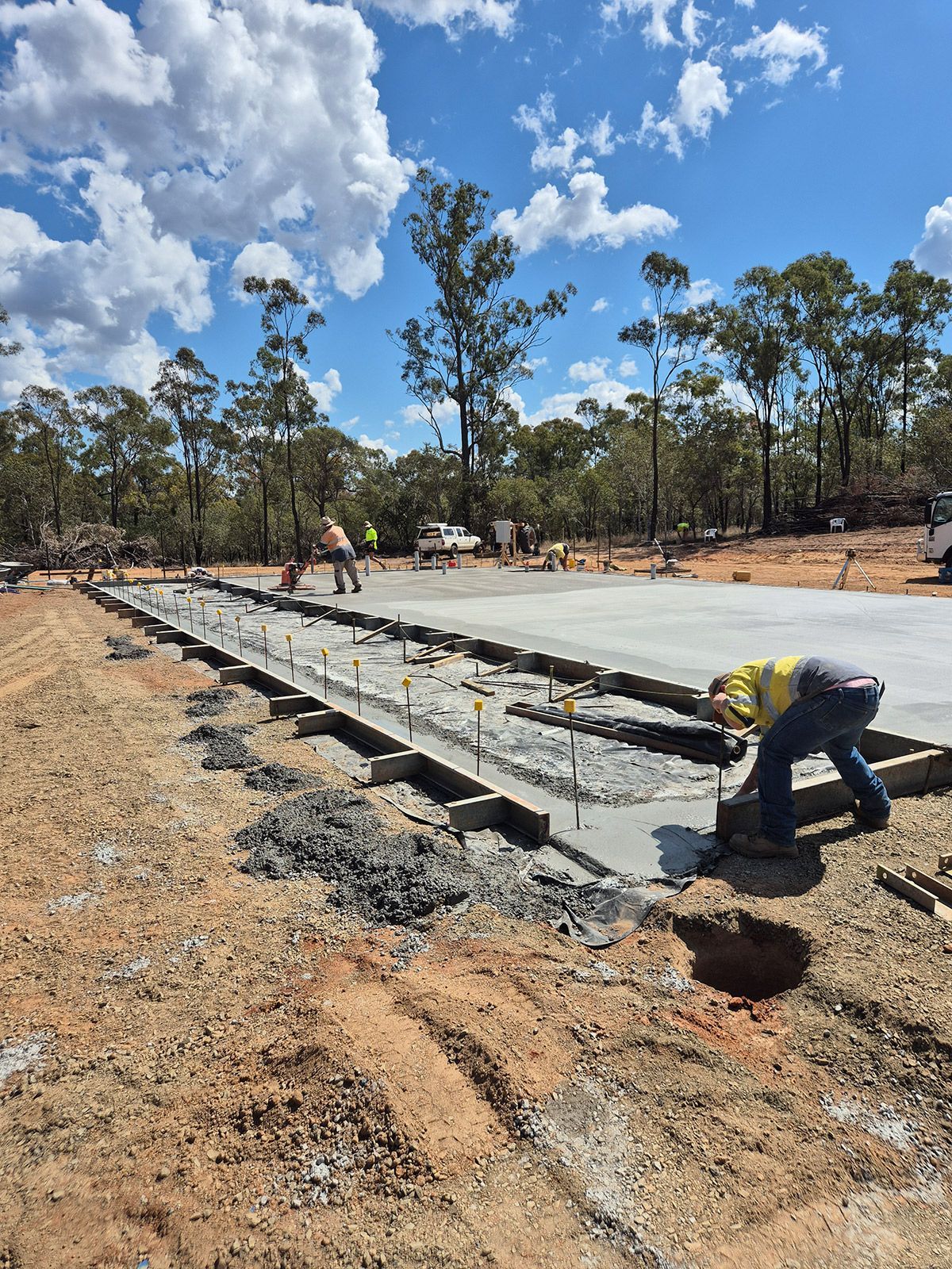 Workers Pour and Finish a Concrete Slab at a Rural Construction Site Under a Blue Sky — TP Concreting In Warilla, NSW