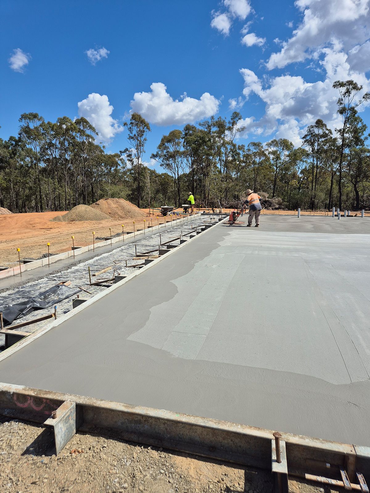 Concrete Slab Being Poured at a Construction Site With Workers, Trees, and a Blue Sky — TP Concreting In Warilla, NSW