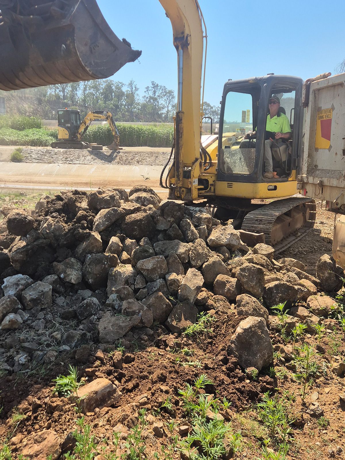Excavator Unloading Large Rocks at a Construction Site Beside a Dirt Road — TP Concreting In Warilla, NSW