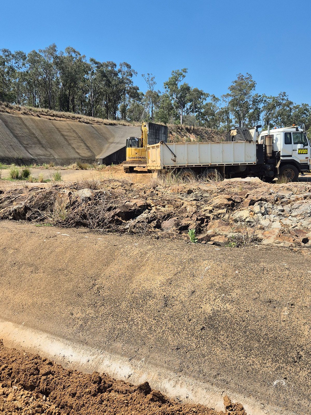 Dump Truck and Excavator on a Dirt Construction Site Beside a Sloped Embankment — TP Concreting In Warilla, NSW