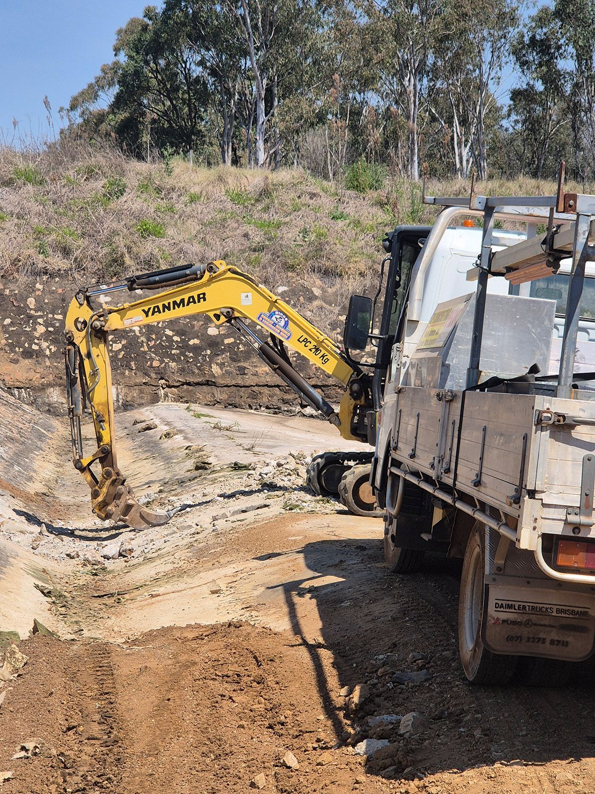 Yellow Excavator Digging Beside a White Truck at a Dirt Construction Site — TP Concreting In Warilla, NSW