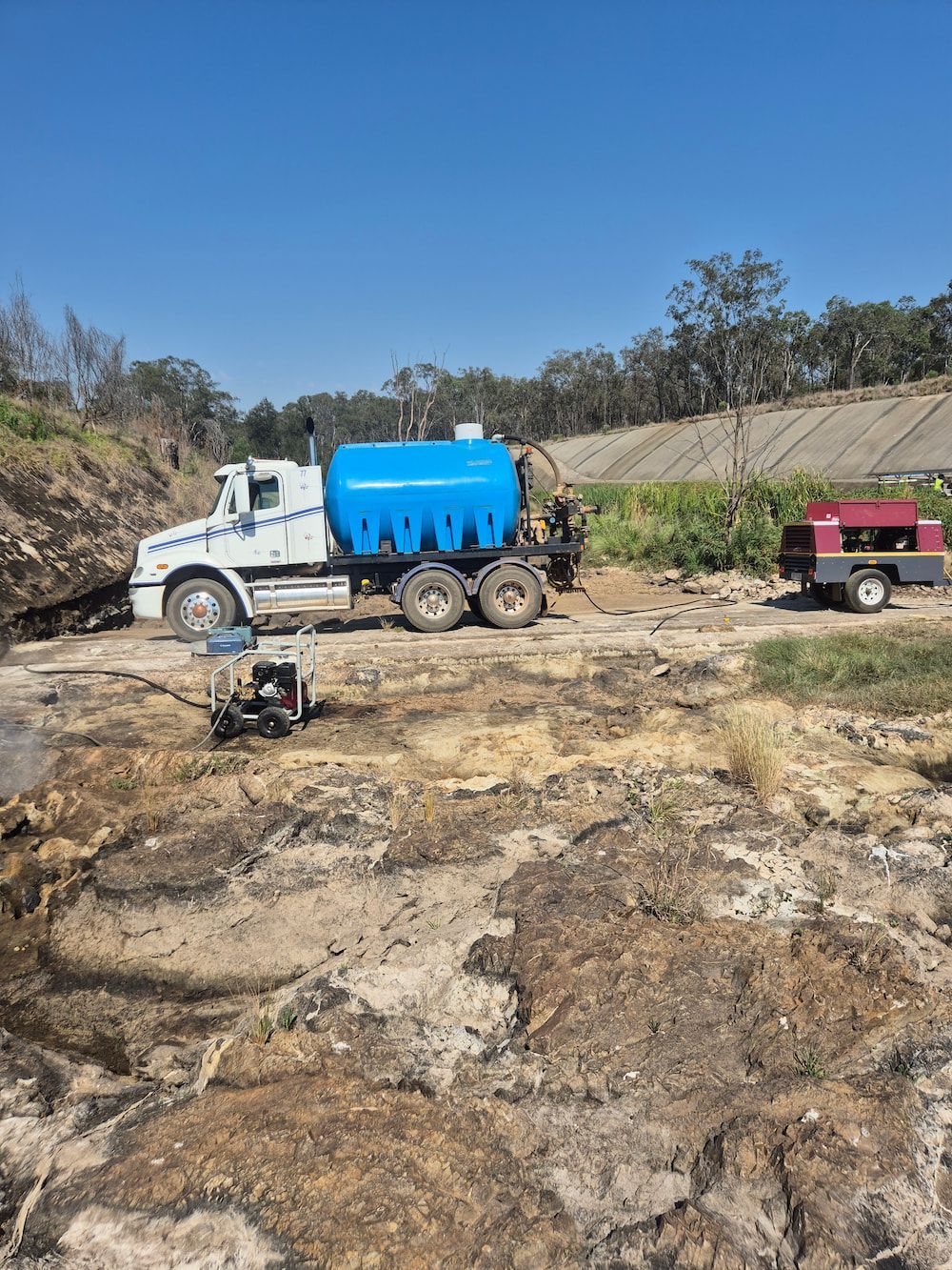 White and Blue Tanker Truck on Rocky Ground With a Red Trailer— TP Concreting In Kingaroy, QLD