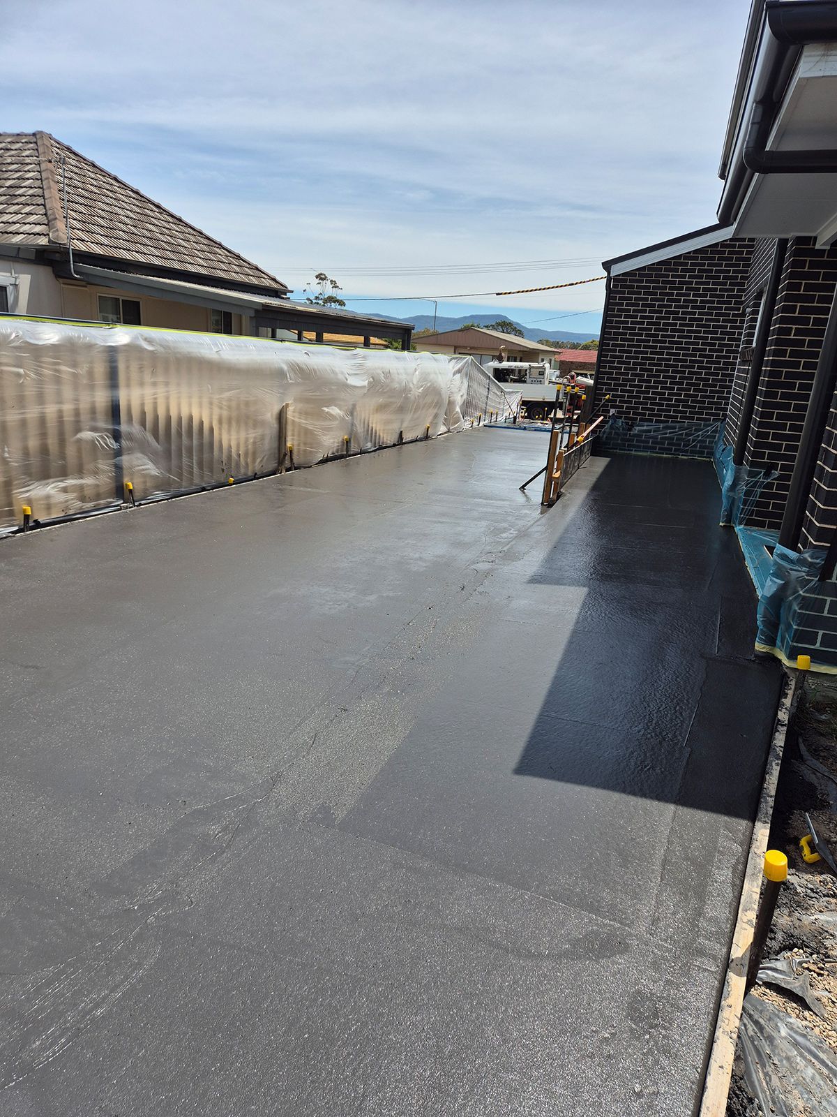 Freshly Paved Black Driveway Beside a Brick House — TP Concreting In Albion Park, NSW