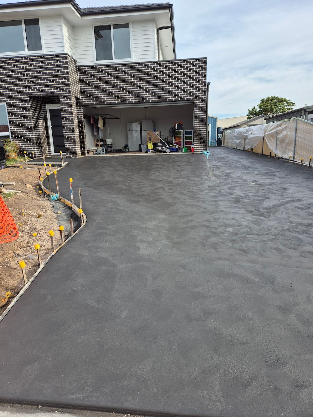 Freshly Paved Black Driveway Beside a Brick House and Garage — TP Concreting In Dapto, NSW